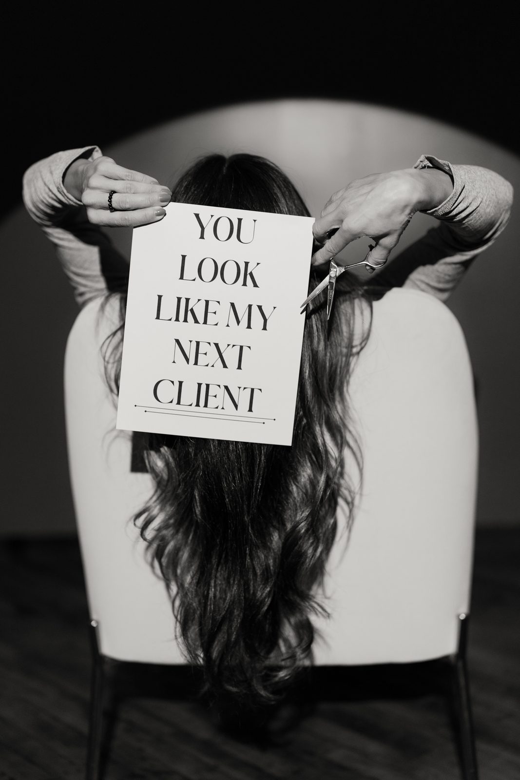 Jessica holding a sign reading “You look like my next client” behind her chair